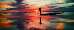 silhouette of person standing on rock surrounded by body of water